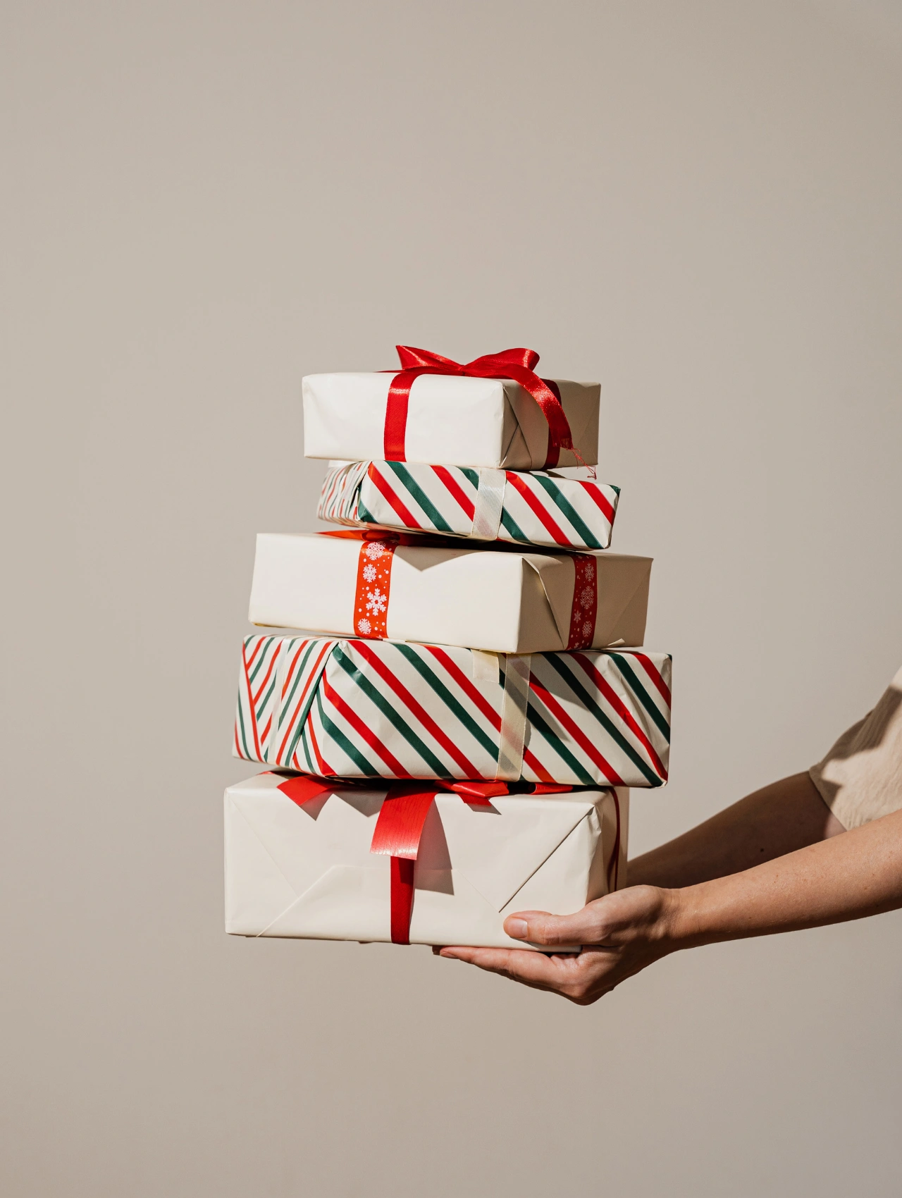 Person holding a tall stack of neatly wrapped presents in minimal holiday colors, emphasizing a clean Christmas aesthetic.