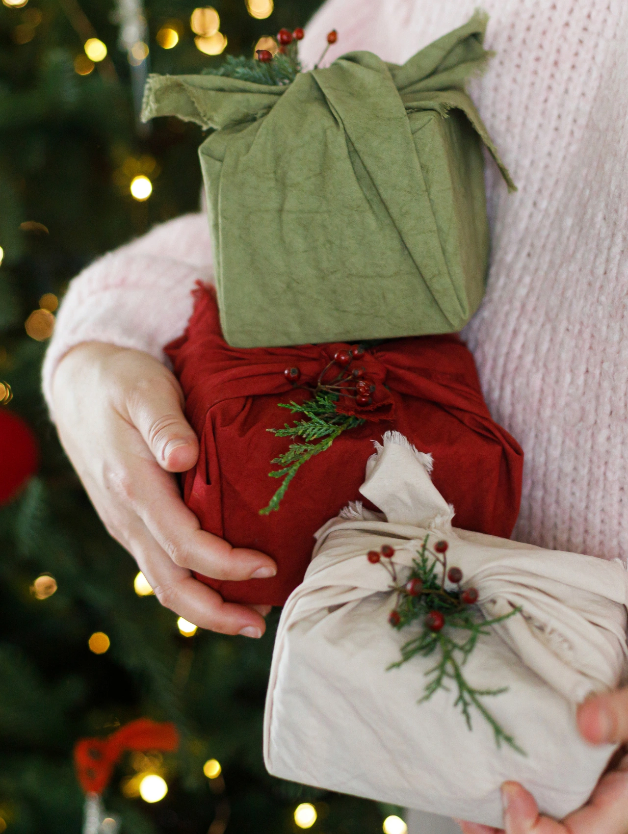 Hands holding eco friendly furoshiki wrapped presents in green, red, and cream fabric, showcasing stylish Last Minute Christmas Gifts