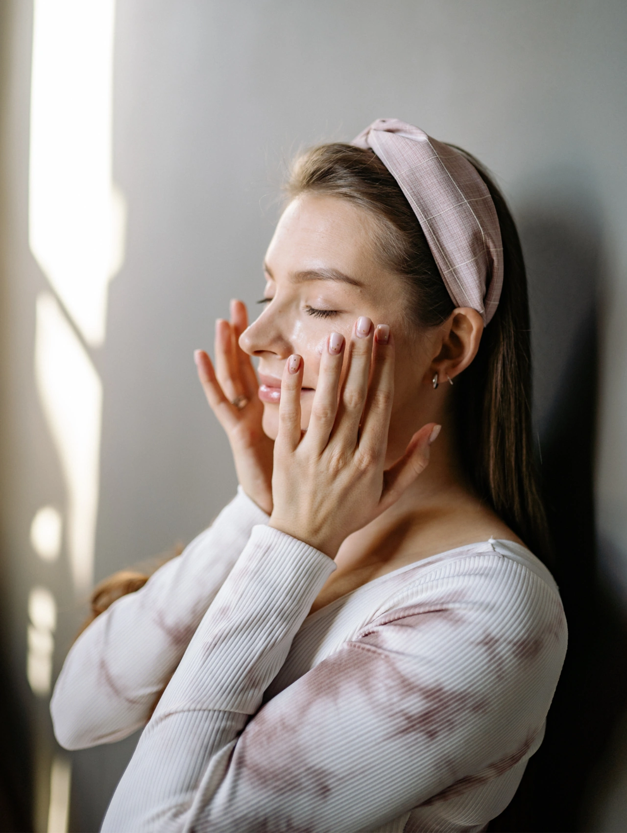 Conclusion for the ultimate skincare, woman gently pressing skincare product into her face by a window, illustrating a calming skincare routine for spring.