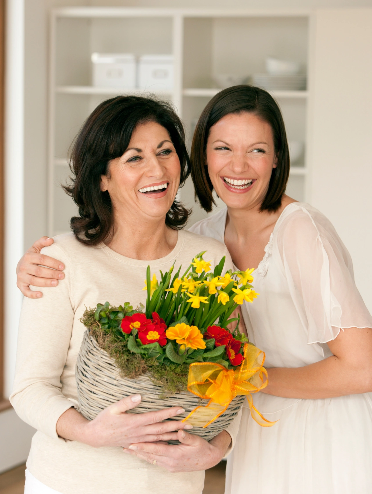 5 Thoughtful Mother’s Day Gift Ideas, smiling mother and daughter hugging indoors while holding a basket of spring flowers, mother's day gift ideas