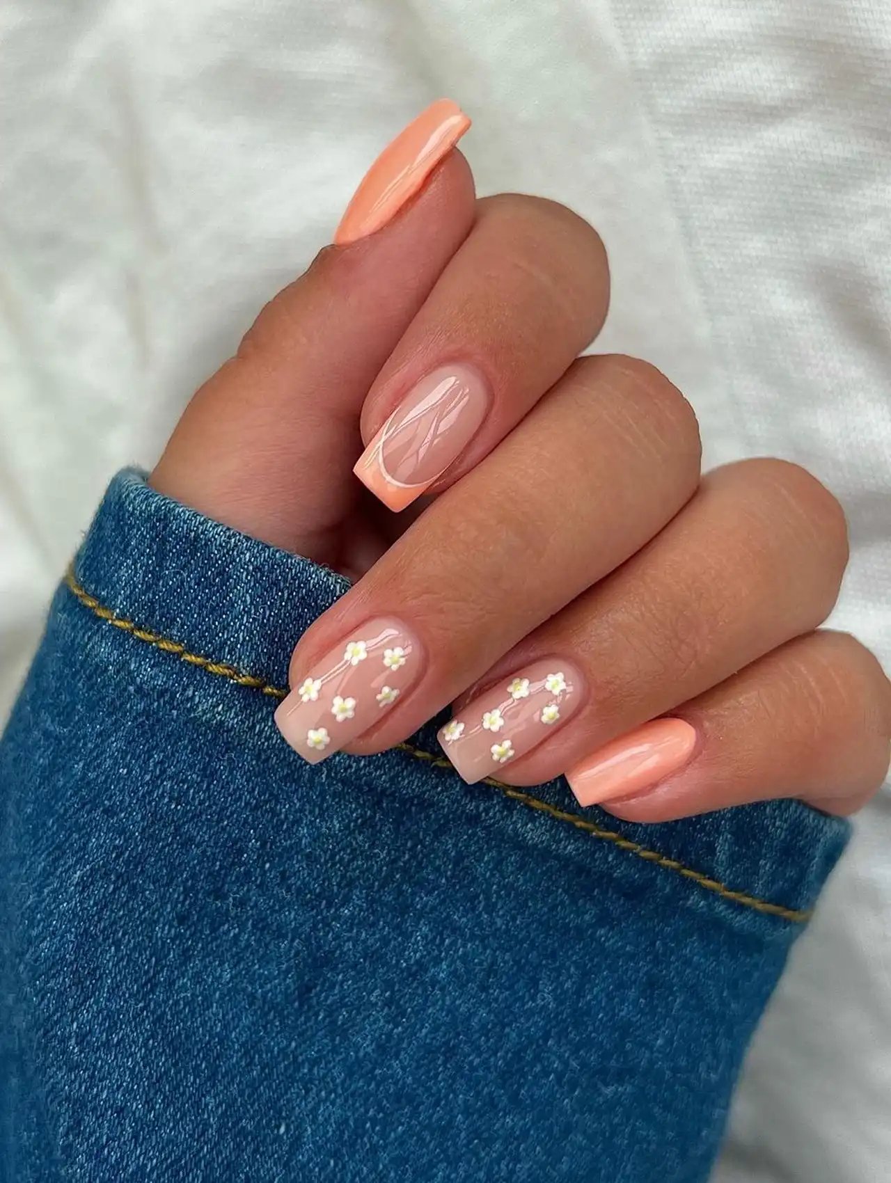 Square nails with peach polish, French tips, and delicate white floral accents, nail art design 2025.