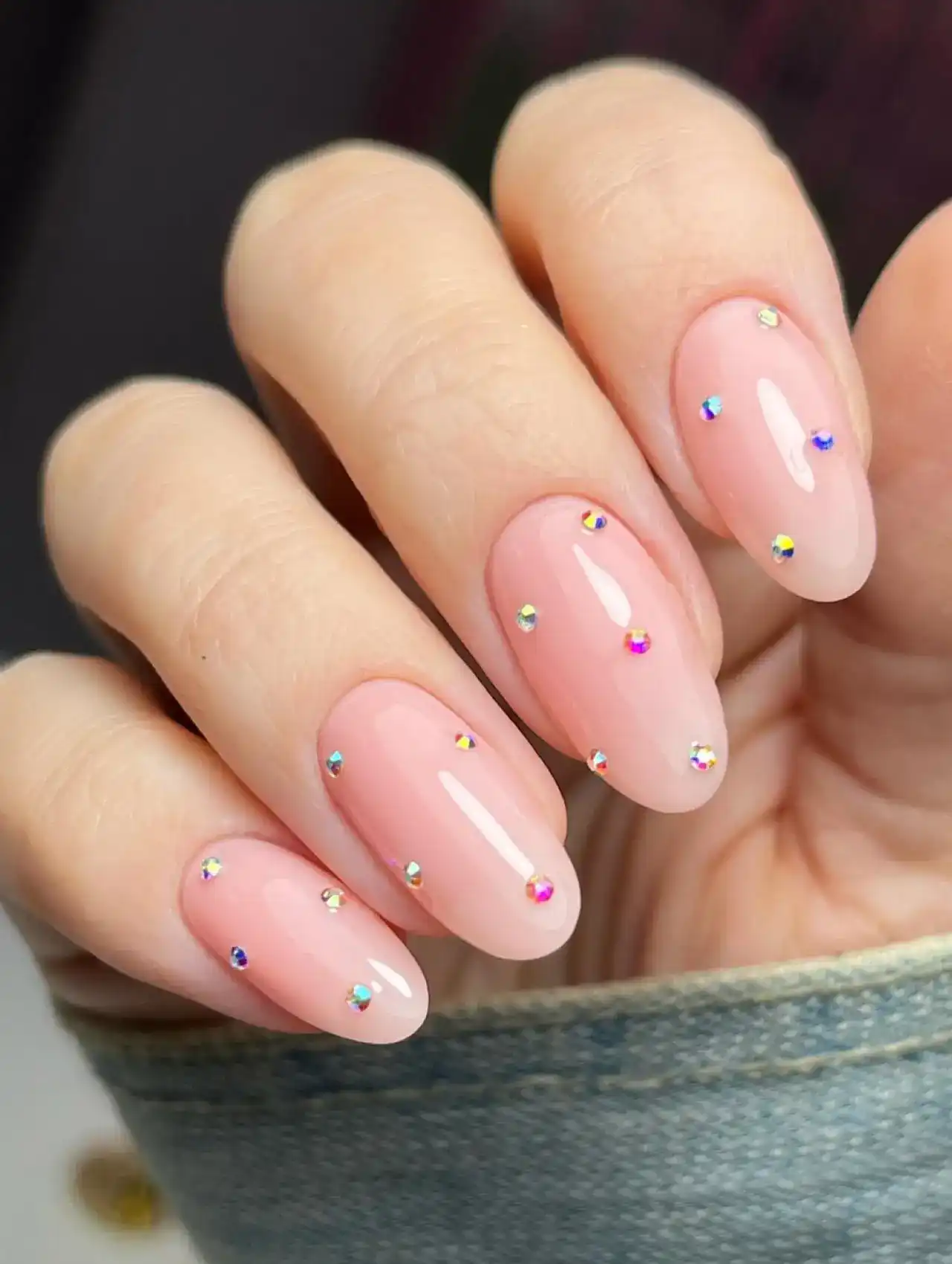 Almond-shaped nude nails with multicolor rhinestone accents, nail art design 2025.
