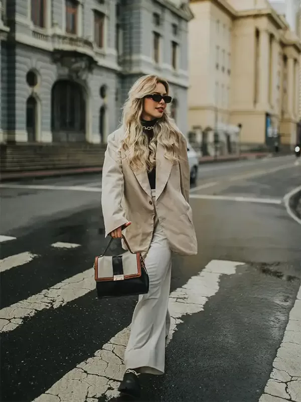a woman wearing sunglasses and a suit holding a purse