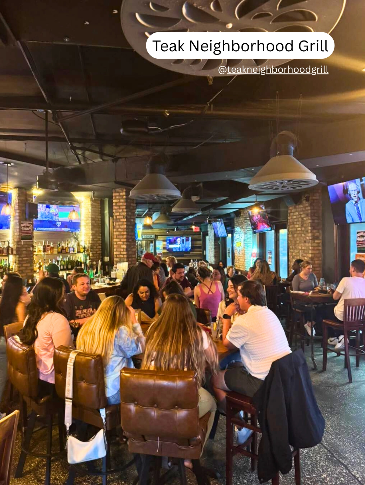 Busy bar and dining area inside Teak Neighborhood Grill with patrons enjoying meals.