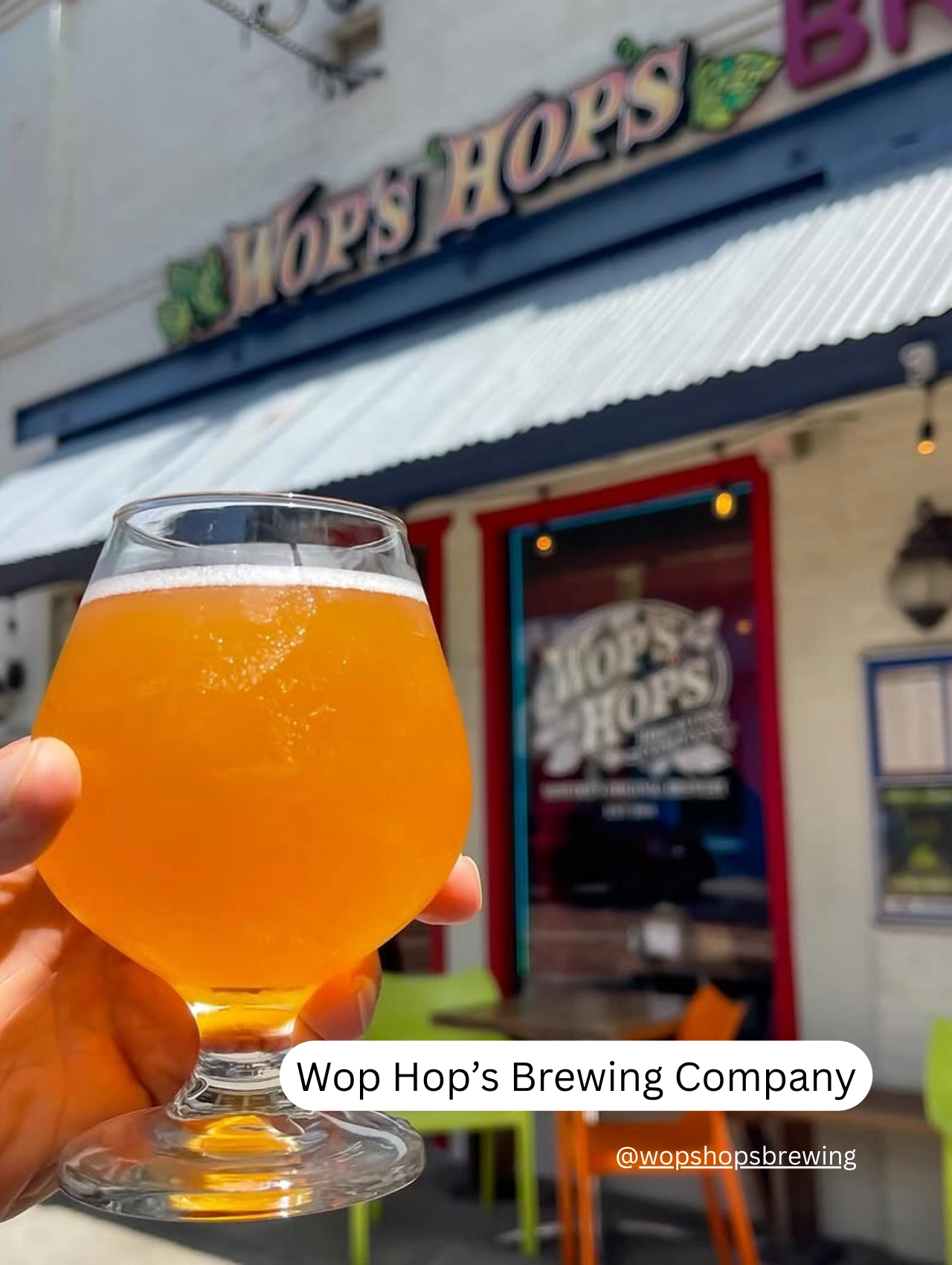 A glass of craft beer held in front of Wop Hop’s Brewing Company in downtown Orlando, a pet friendly restaurant with outdoor seating.
