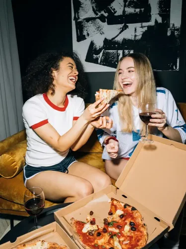 two women sitting on a couch eating pizza