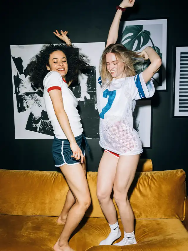 two women in sports uniforms jumping on a couch
