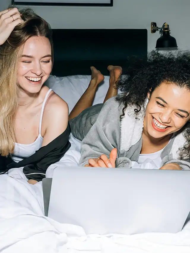 two women lying on a bed looking at a laptop