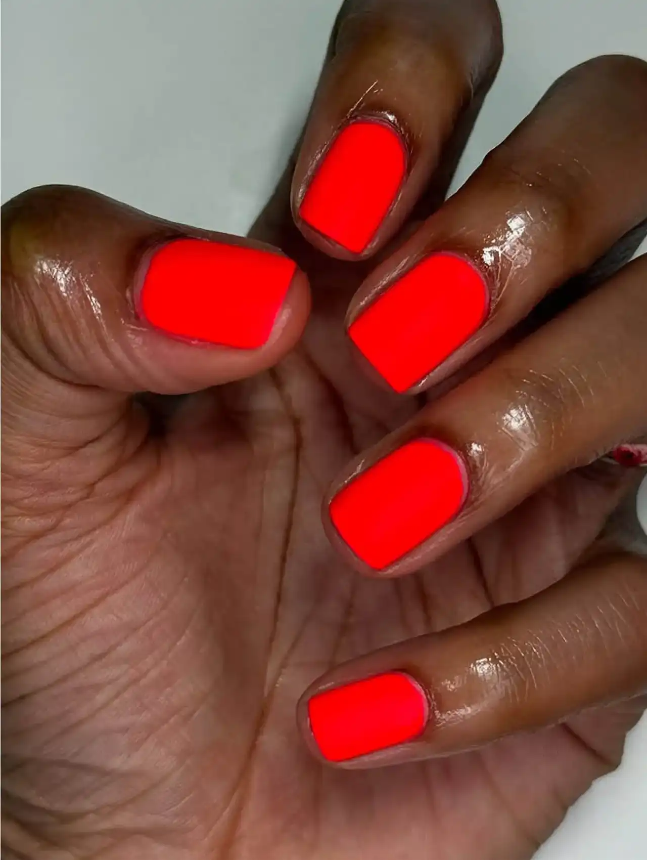 Close-up of matte red neon nails on square-shaped manicure