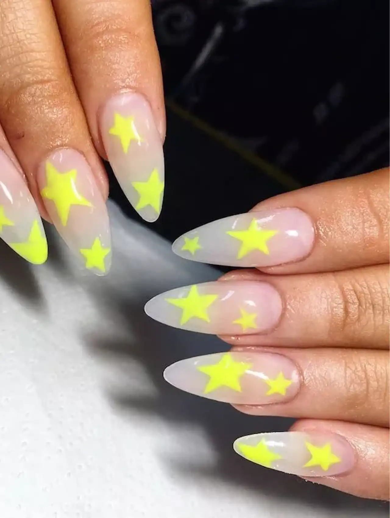 Long almond-shaped neon nails with bright yellow star designs