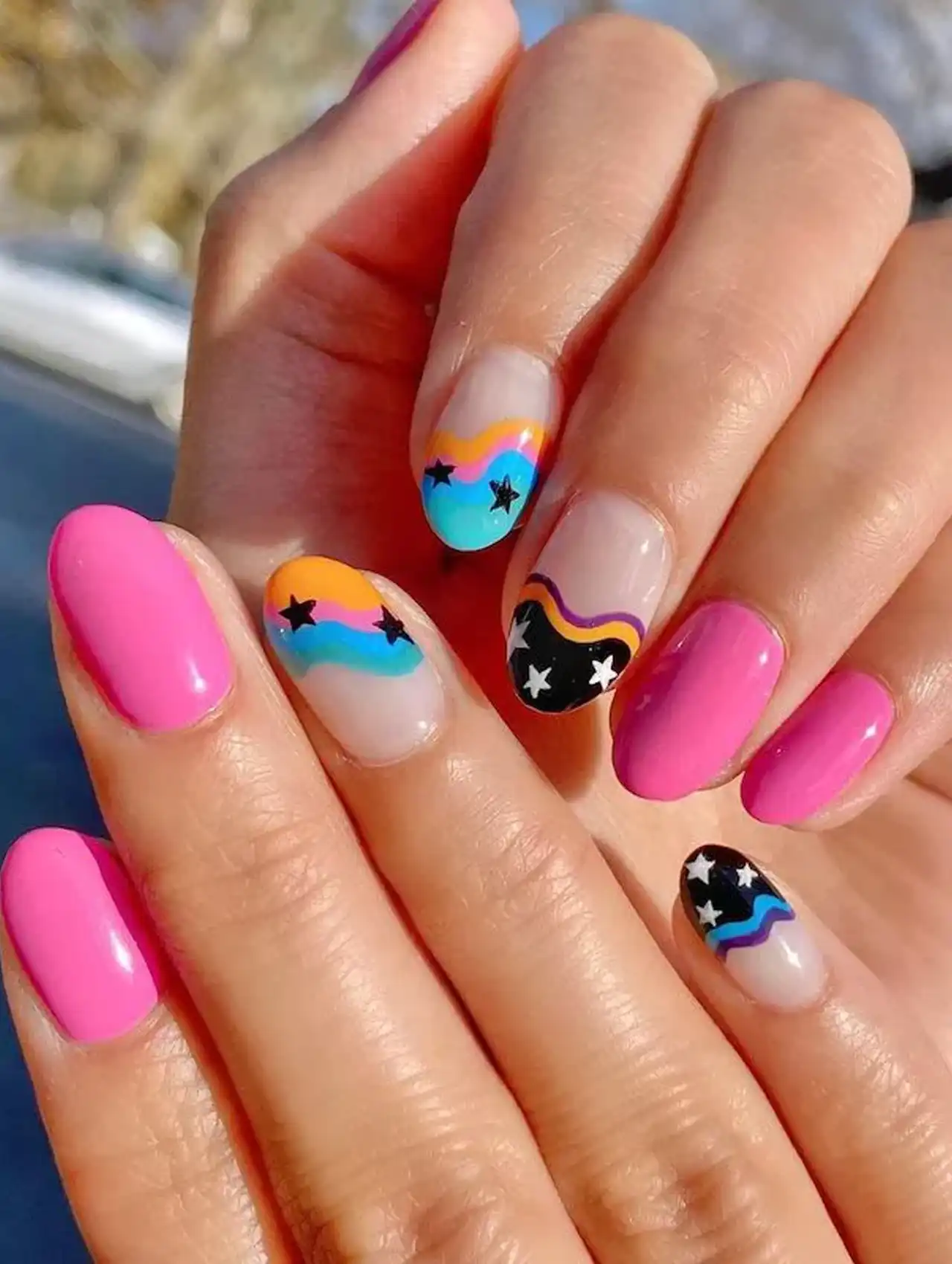 Neon nails with pink polish, colorful waves, and black star accents