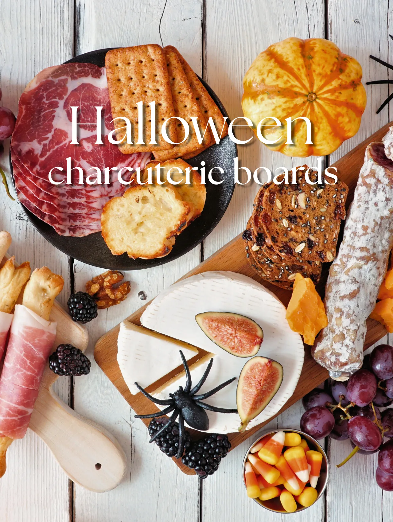 Overhead halloween charcuterie board with prosciutto, salami, brie, figs, candy corn and a toy spider on white wood