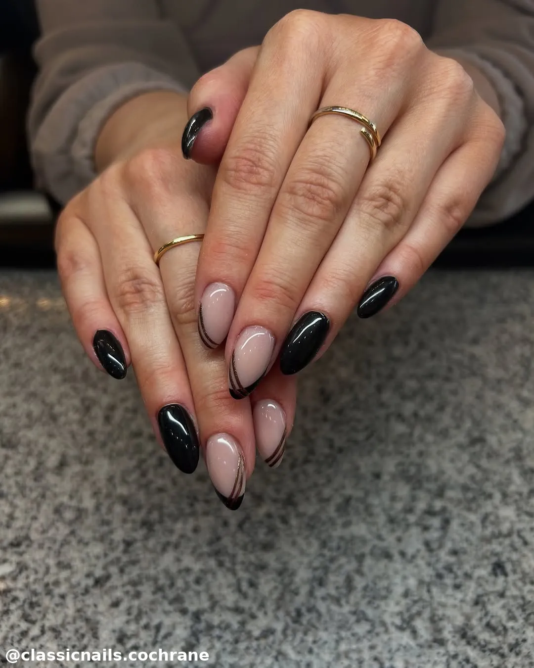 Uñas acrílicas almendradas con esmalte negro, nude y líneas curvas decorativas