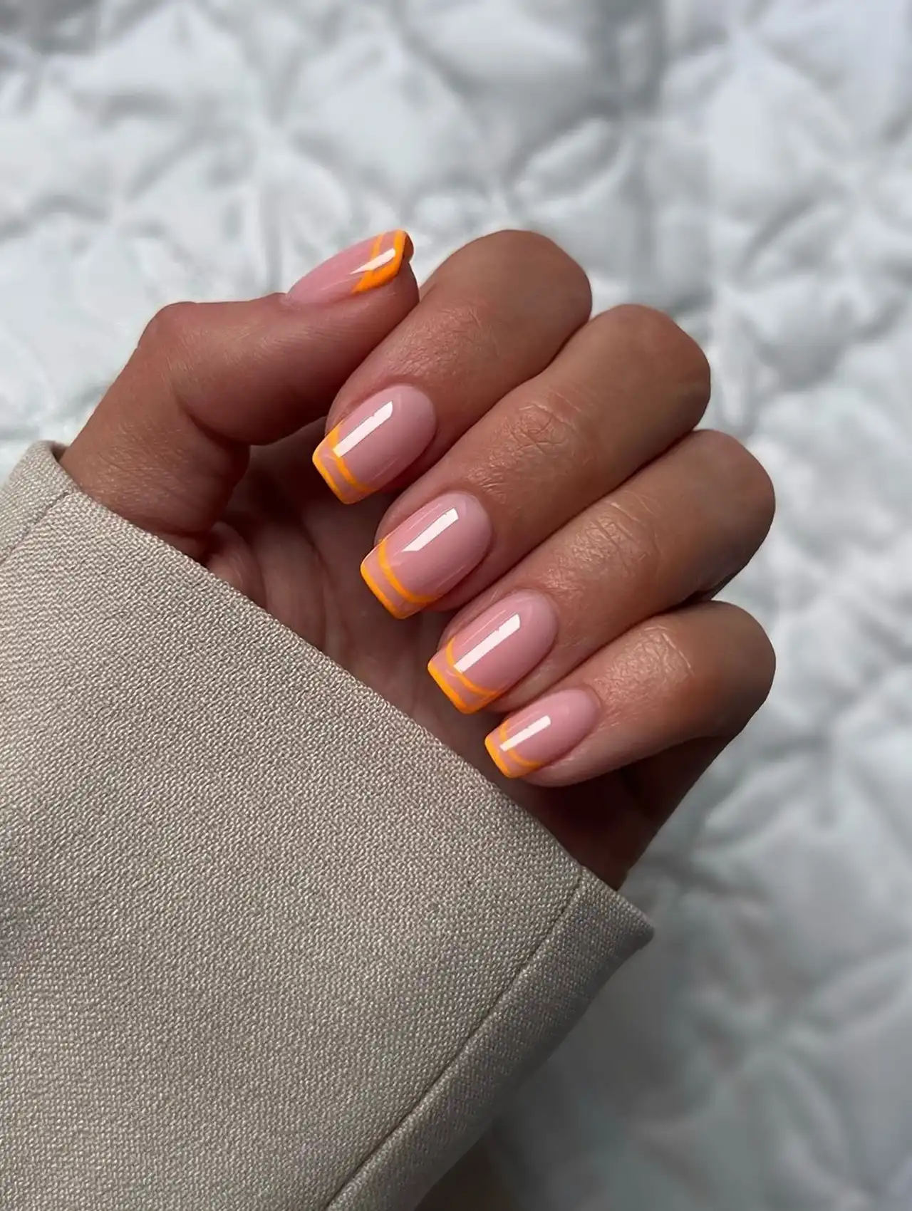 Hand with Aperol-inspired orange French tips, perfect for summer nail designs