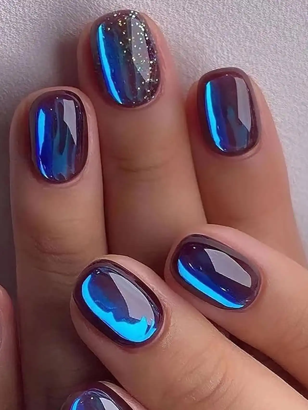 Blue chrome reflective nails with glitter accent showcasing aurora nail design ideas