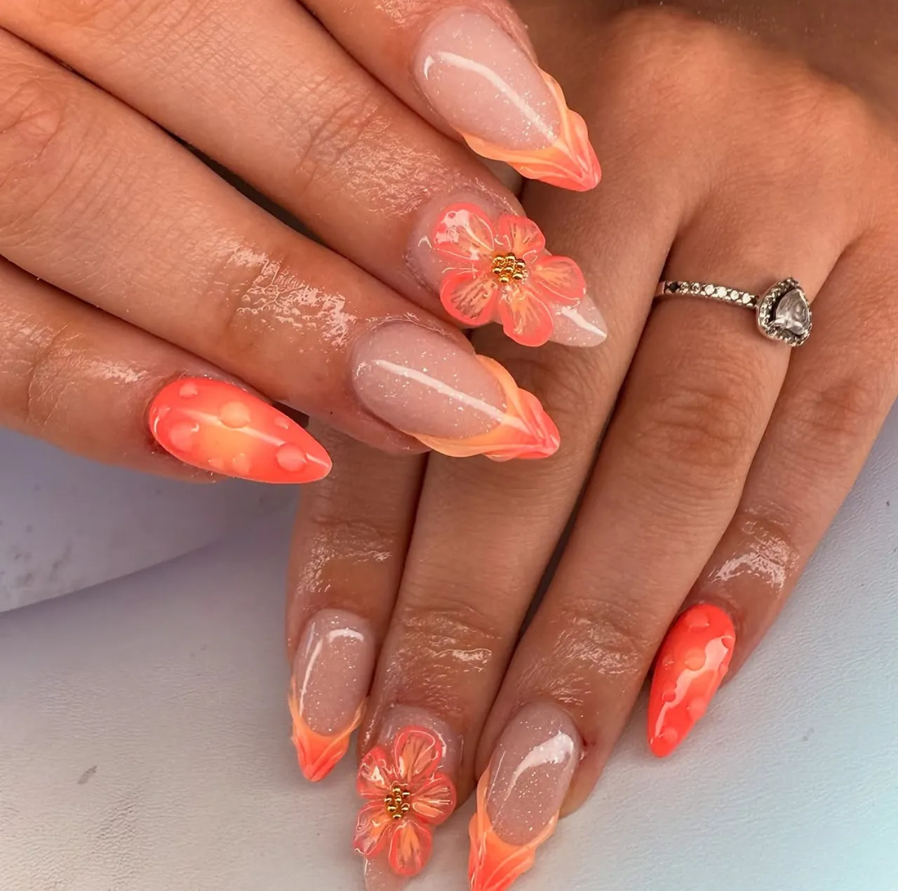 Diseño de uñas con arte de uñas en 3D en tonos coral y detalles florales.