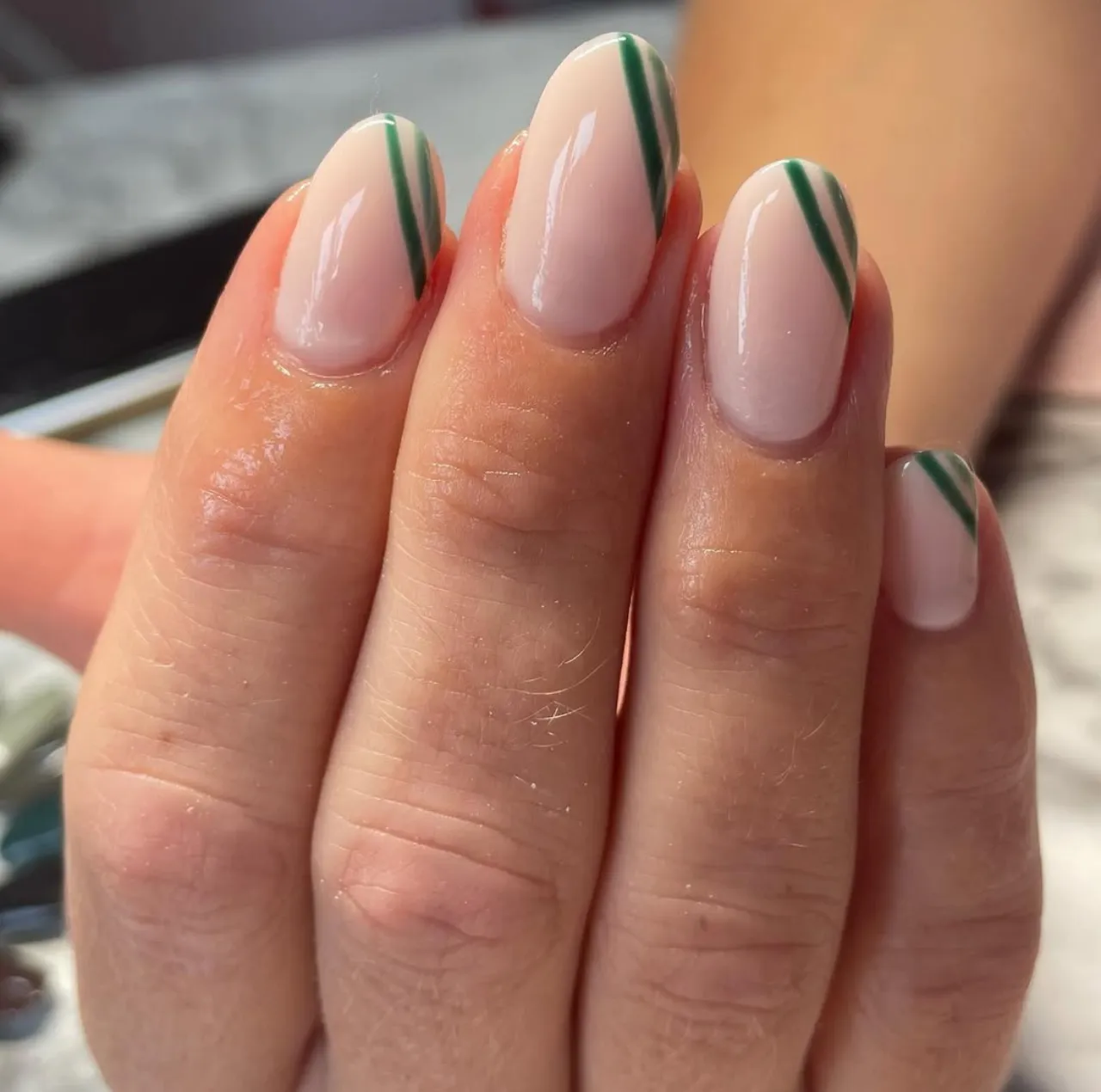 Diseño de uñas con cinta de rayas verdes sobre base nude.