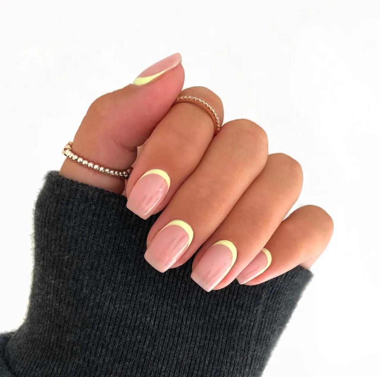 Diseño de uñas con manicura francesa inversa en tono nude y detalle amarillo pastel.