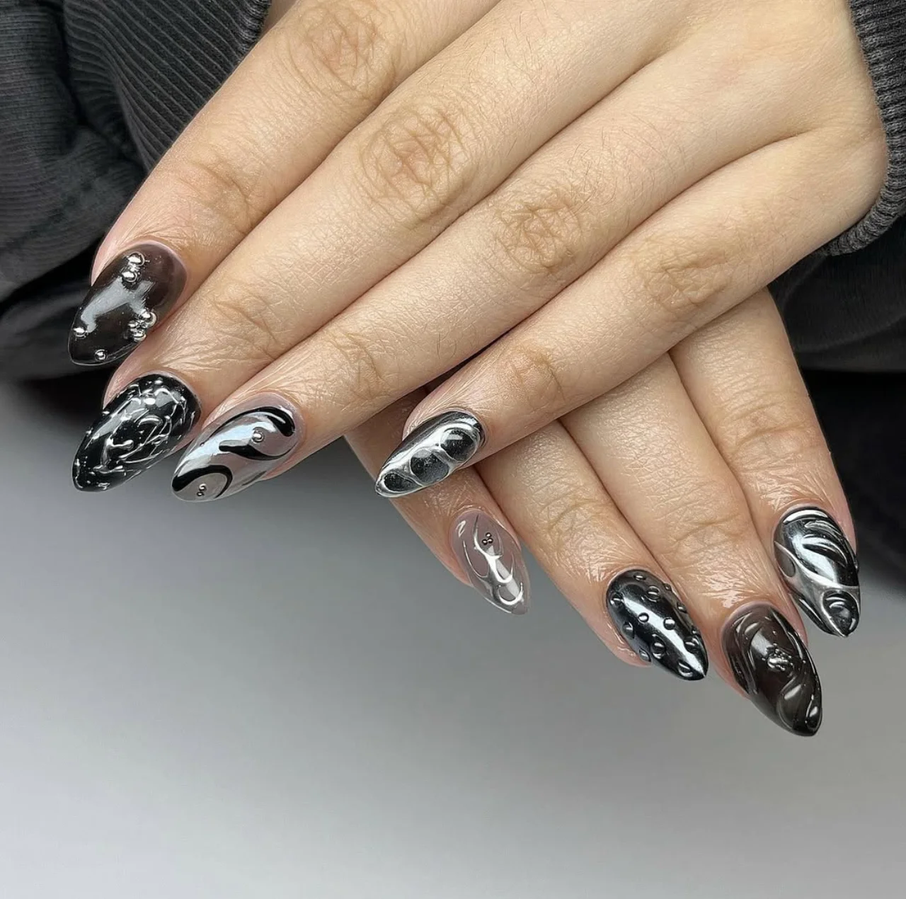 Diseño de uñas negro y plateado con efecto tridimensional y detalles modernos.