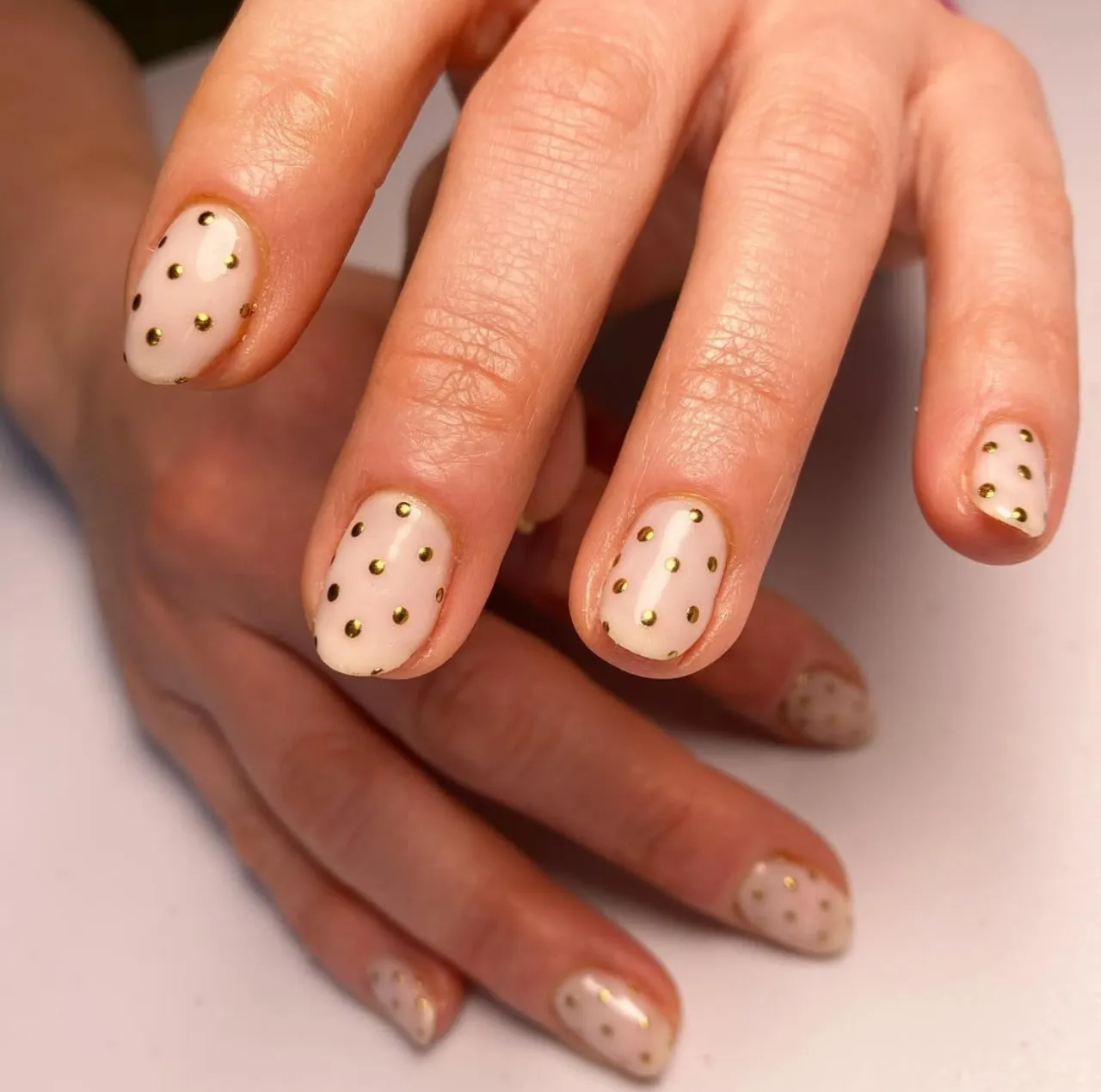 Diseño de uñas con piedras y tachuelas doradas sobre base nude.