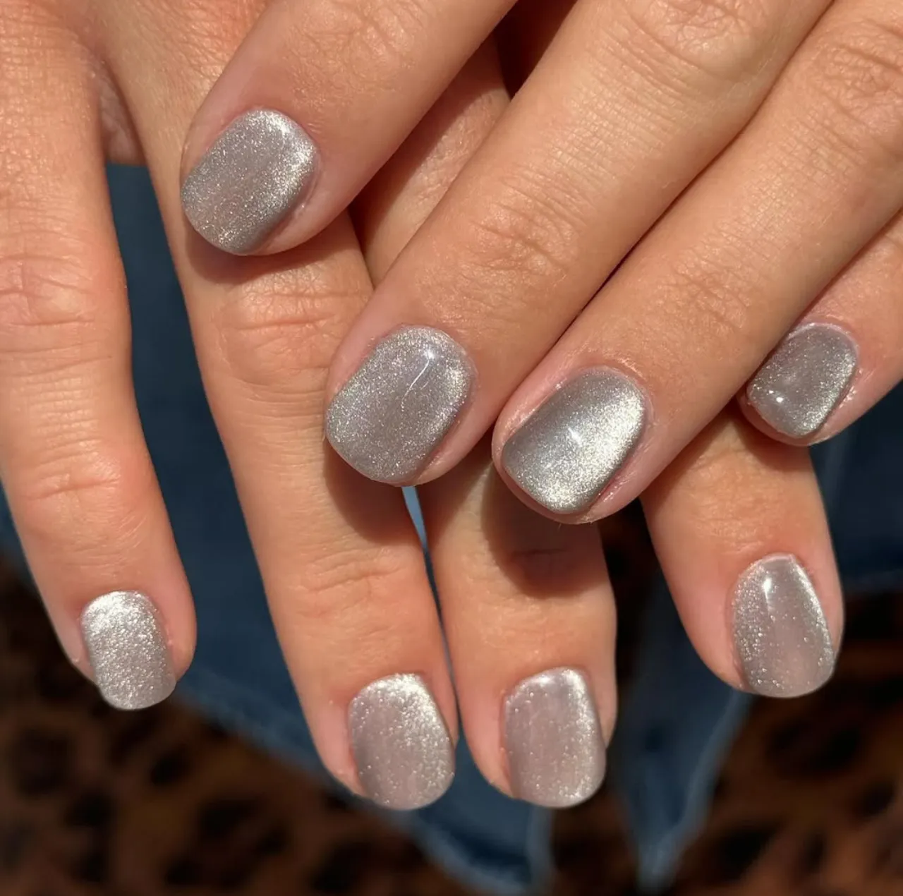 Diseño de uñas con polvo aterciopelado plateado sobre uñas cortas.