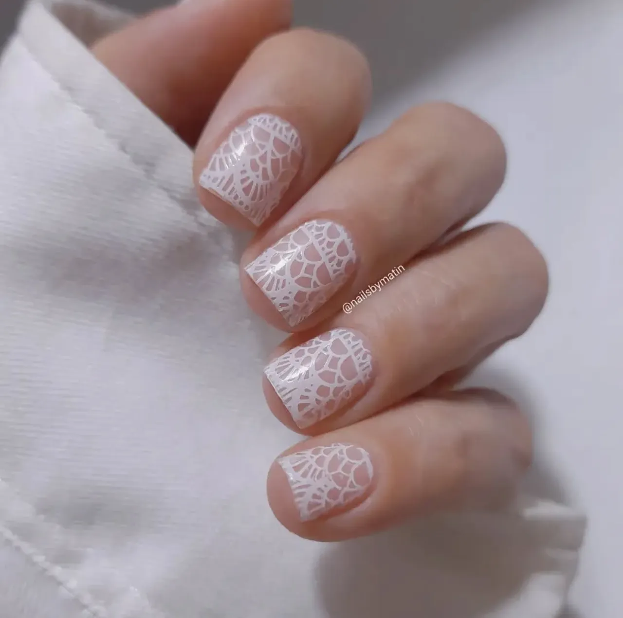 Diseño de uñas de encaje blanco sobre fondo nude en uñas cortas.