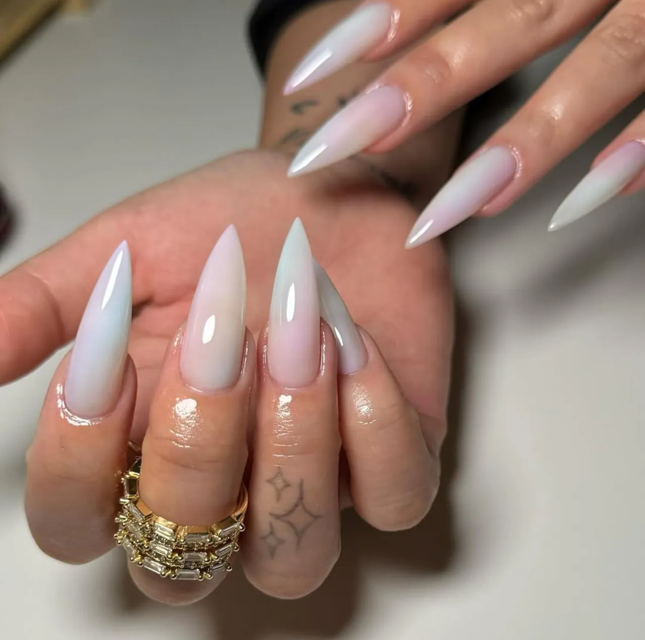 Diseño de uñas estileto en tonos nude con acabado brillante y forma puntiaguda.