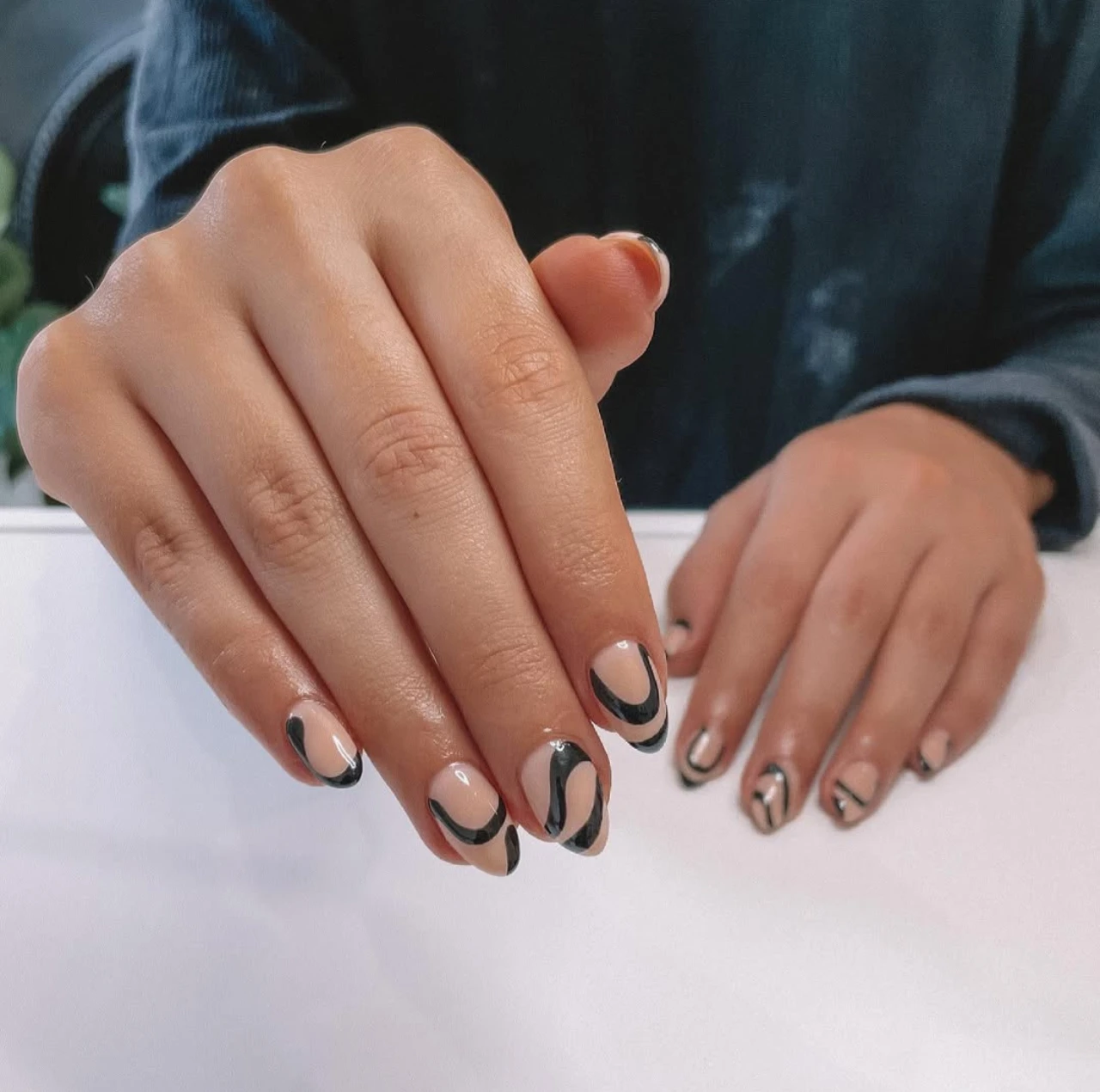 Diseños de uñas acrílicas abstractas con patrón negro sobre base nude.