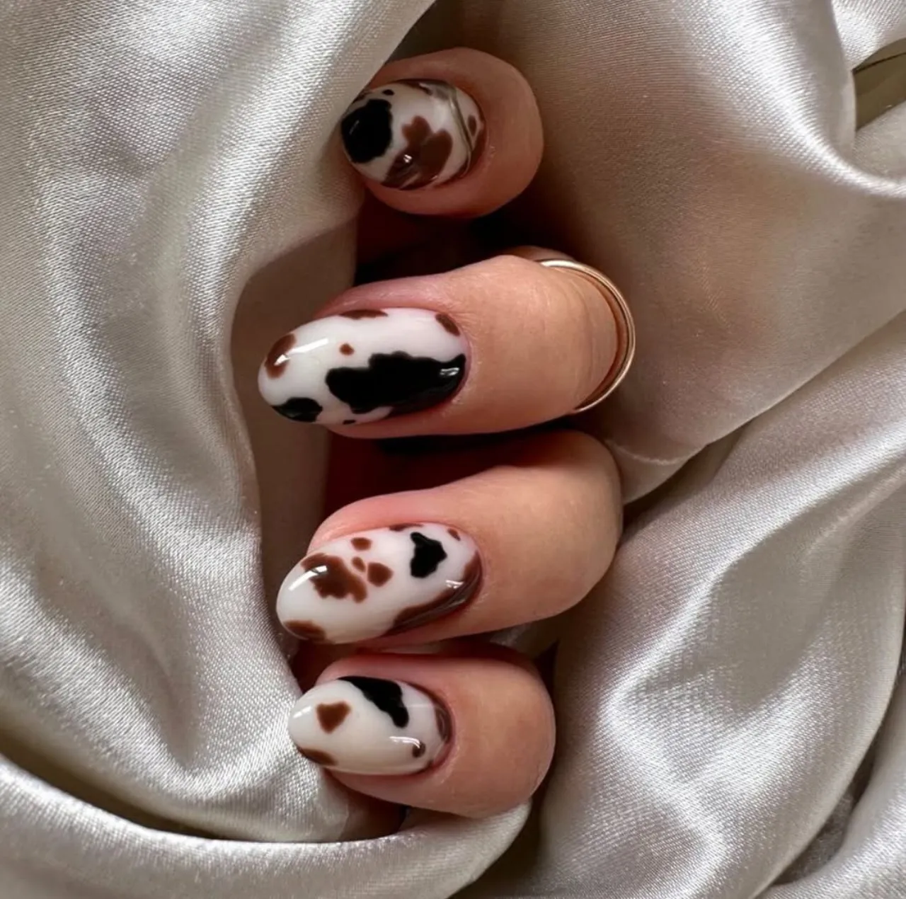 Diseños de uñas acrílicas de vaca con manchas en tonos marrón y negro sobre fondo blanco.