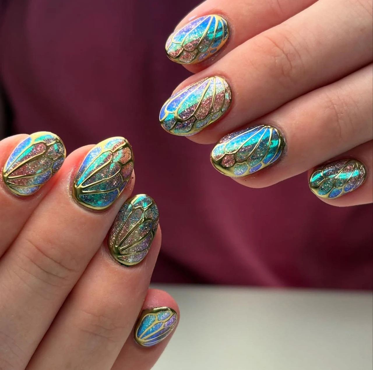 Diseños de uñas acrílicas estilo fairy con detalles tornasolados y líneas doradas.