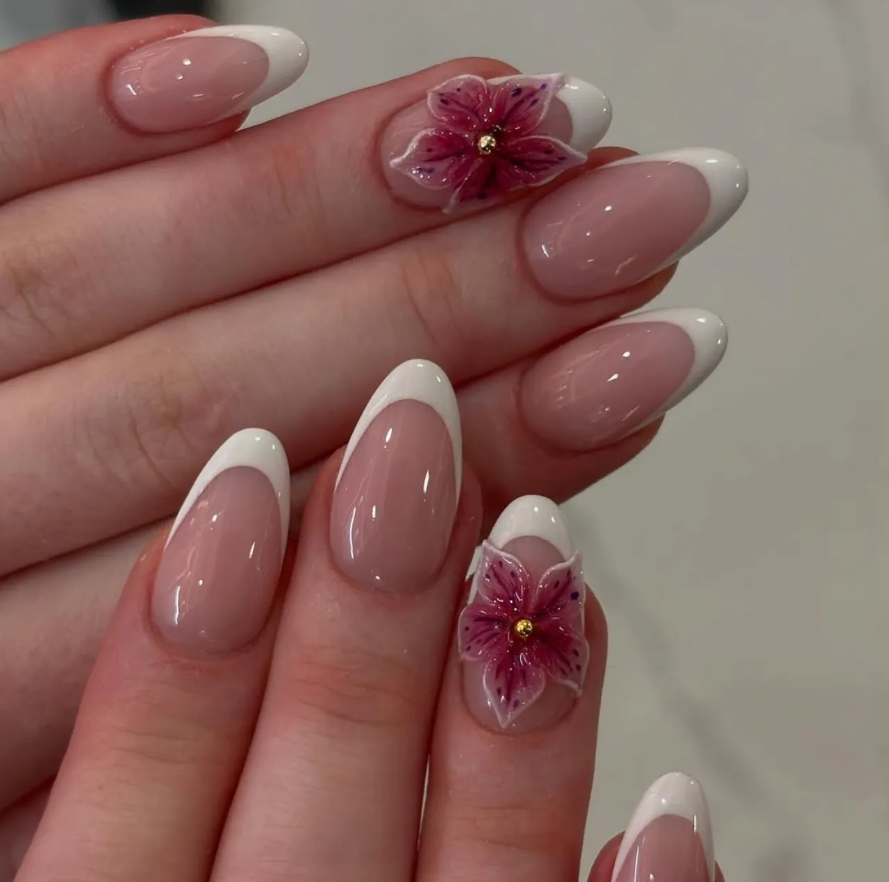 Diseños de uñas acrílicas con flores 3D acrílicas en color rosa sobre base francesa clásica.