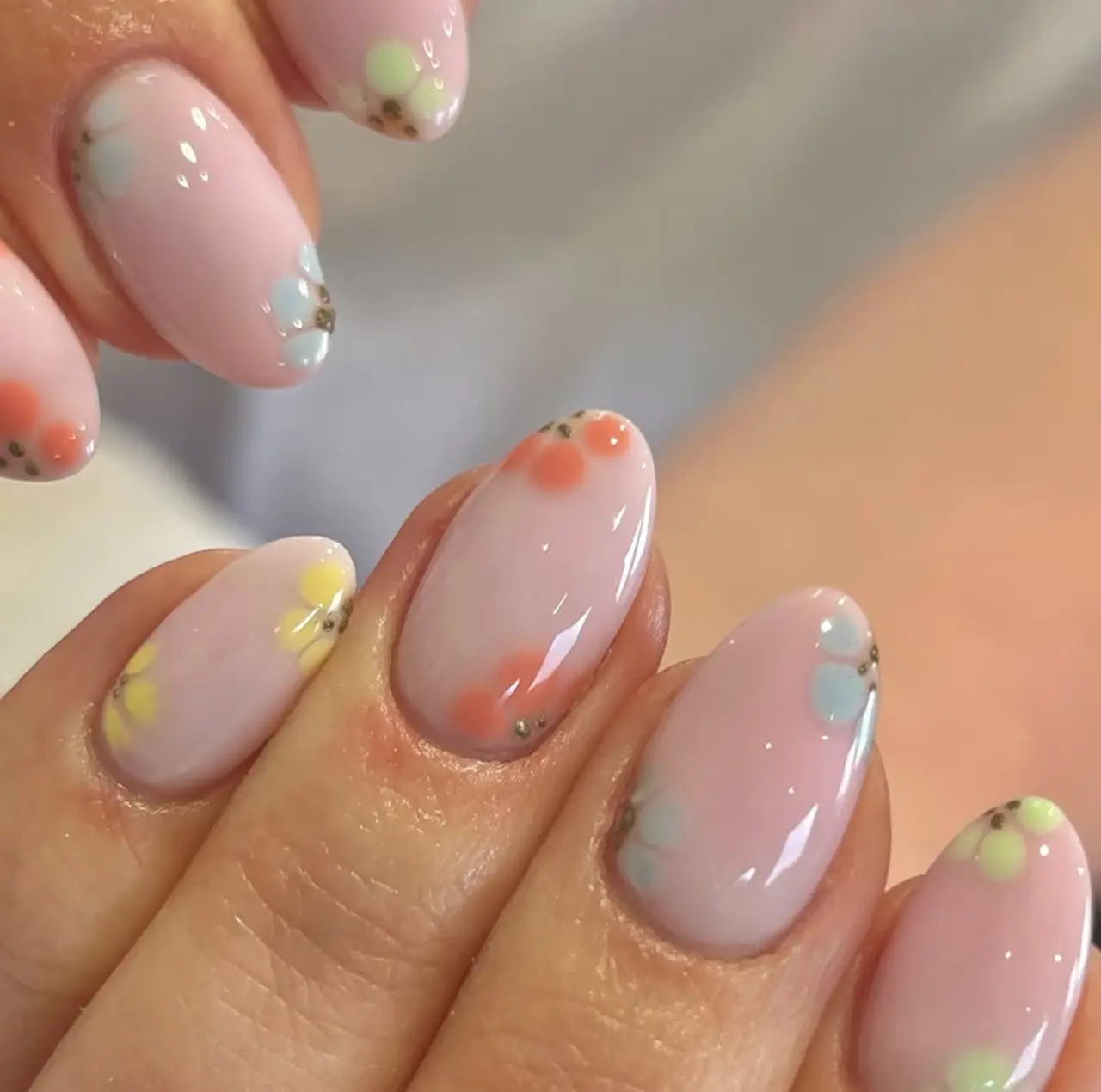 Diseños de uñas acrílicas con flores en tonos cálidos como amarillo, coral y verde sobre base rosa pastel.