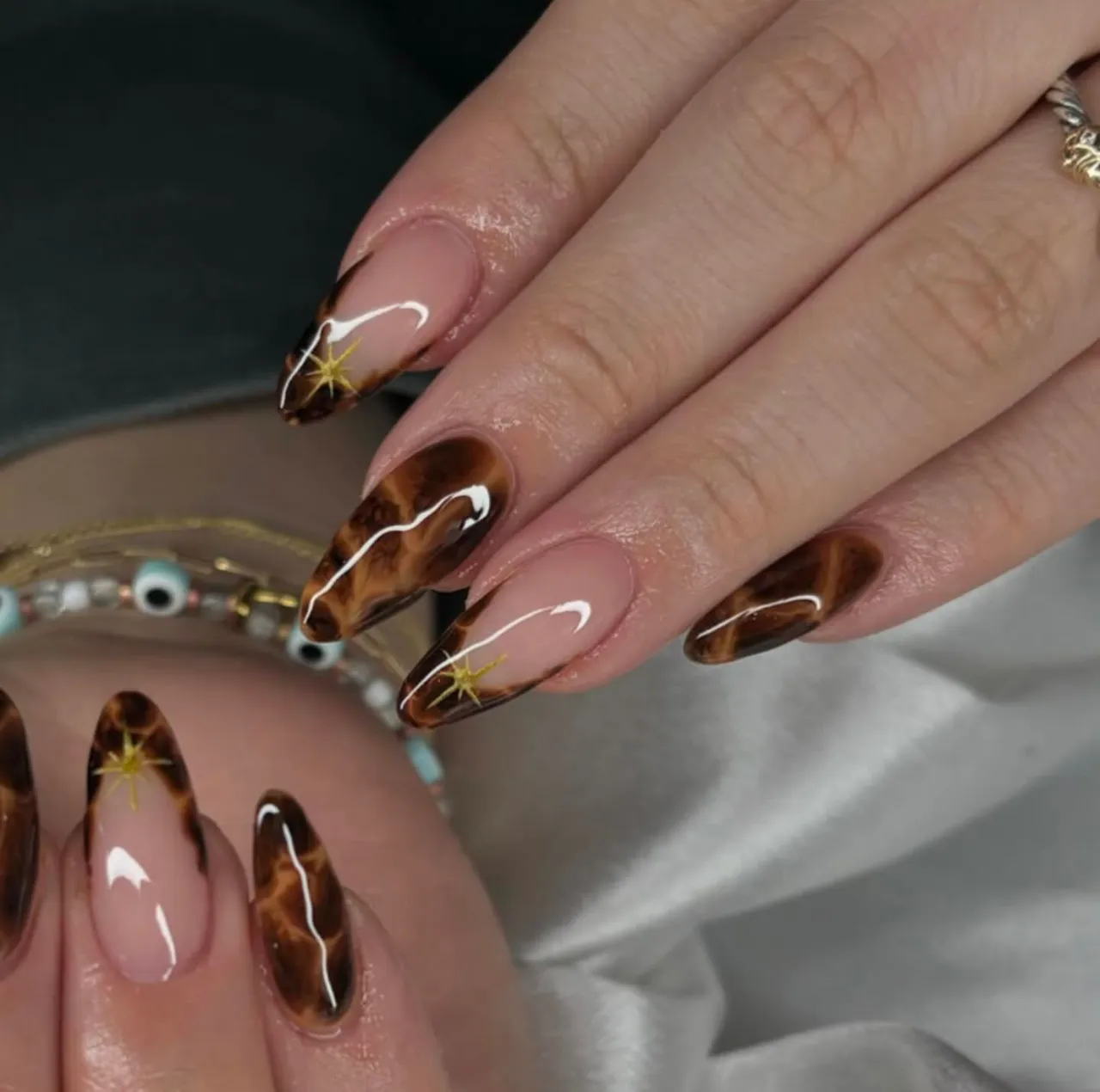 Diseños de uñas acrílicas francesas con estampado tipo leopardo en tonos marrón y dorado.