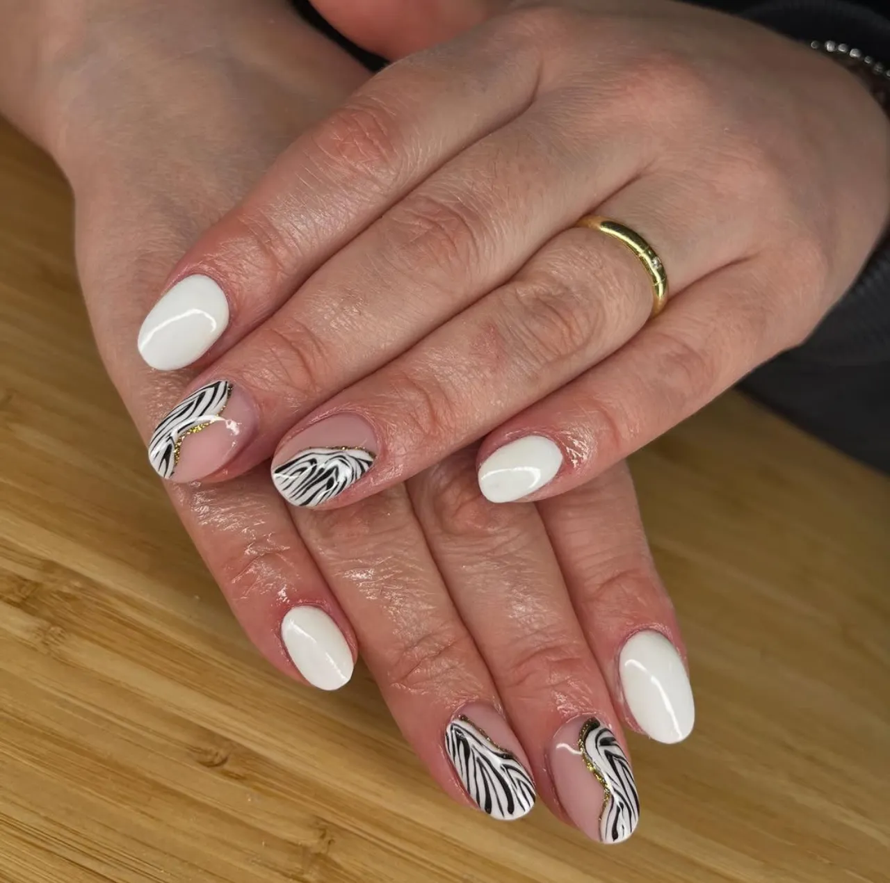 Diseños de uñas acrílicas francesas con estampado de zebra en blanco y negro y detalles dorados.