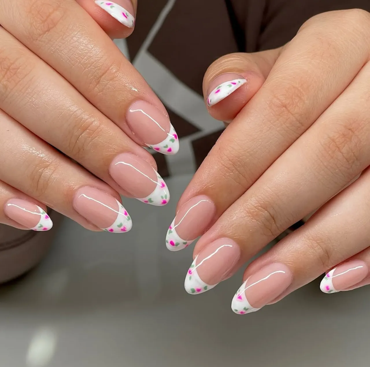 Diseños de uñas acrílicas francesas con flores en tonos rosa y verde sobre base blanca.