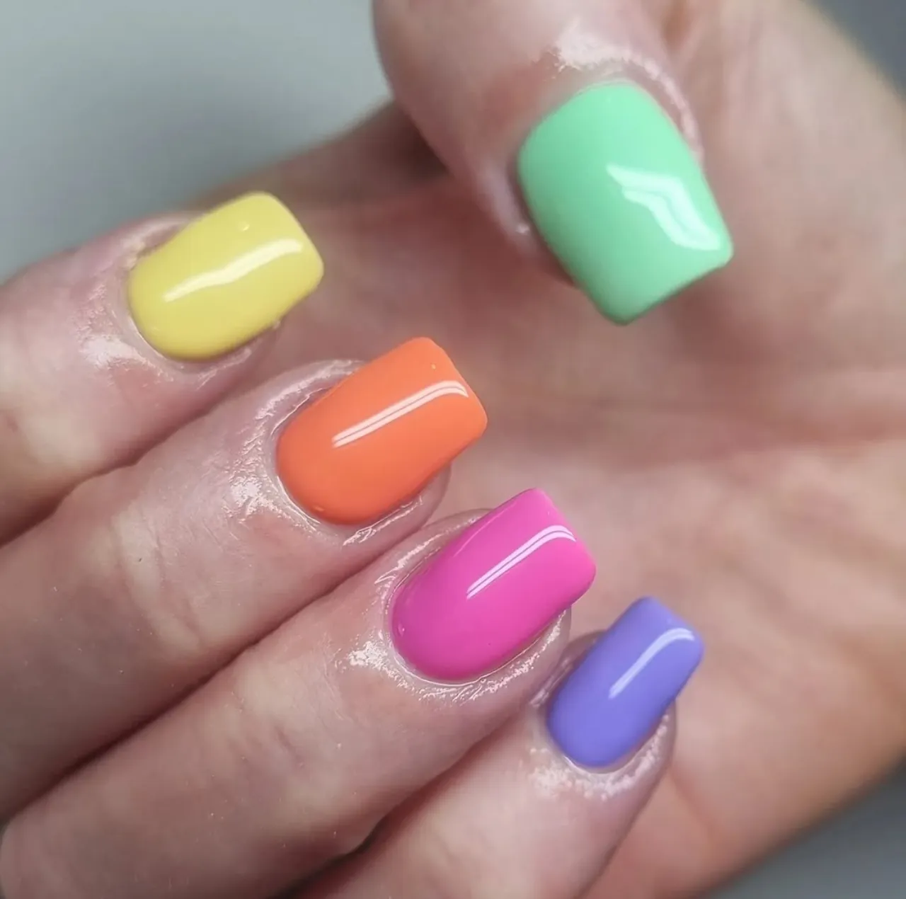 Diseños de uñas acrílicas multicolor en tonos pastel con acabado brillante y forma cuadrada.