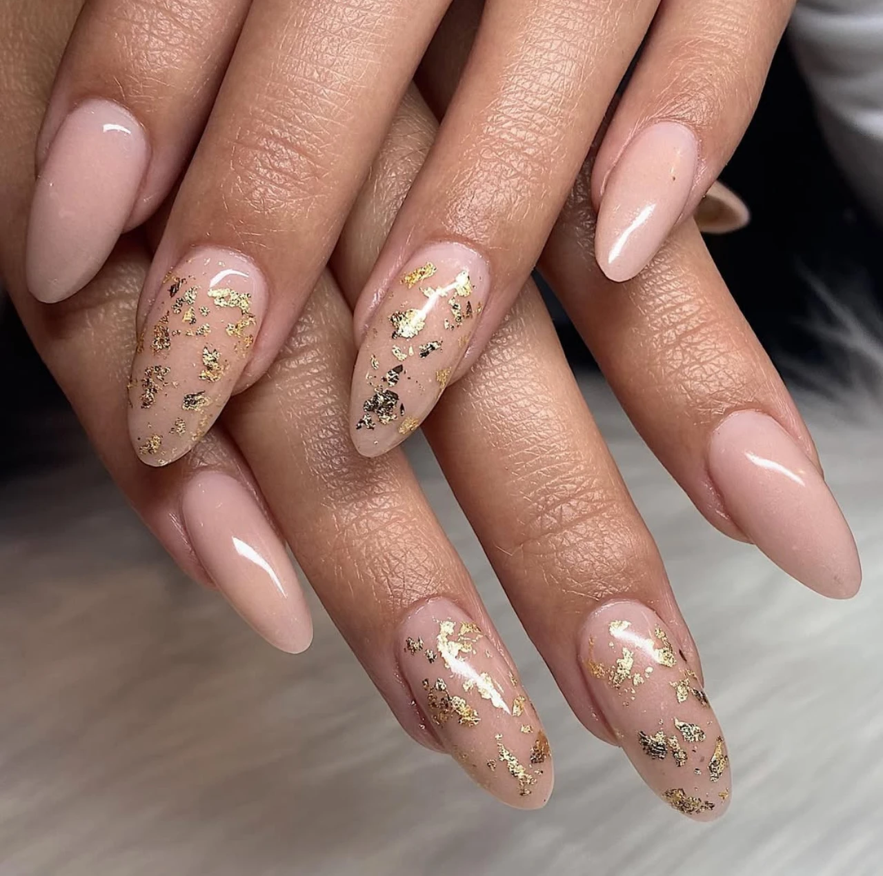 Diseños de uñas acrílicas nude con detalles dorados en acabado brillante.