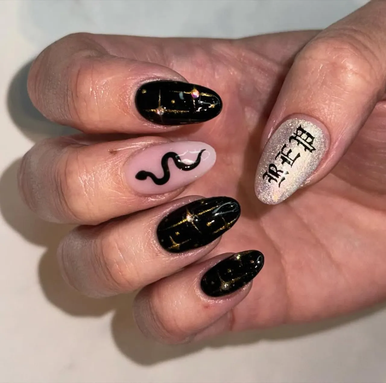 Diseños de uñas acrílicas inspirados en el estilo Reputation de Taylor Swift con tonos negro, dorado y detalles góticos.