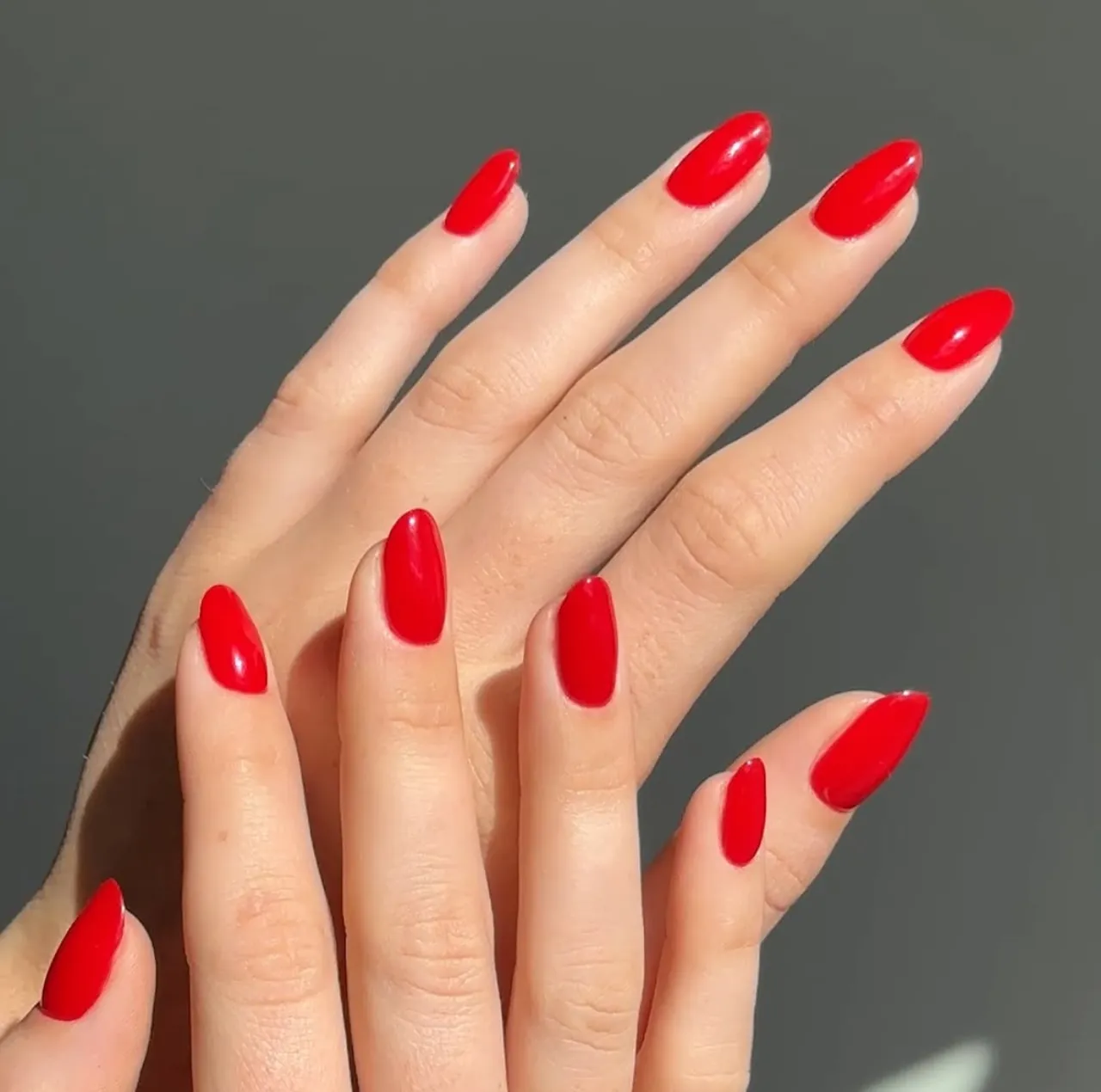 Diseños de uñas acrílicas rojas tradicionales con forma almendrada y acabado brillante.
