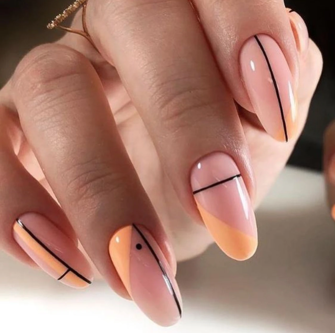 Diseños de uñas acrílicas largas con diseño abstracto en tonos durazno y líneas negras.