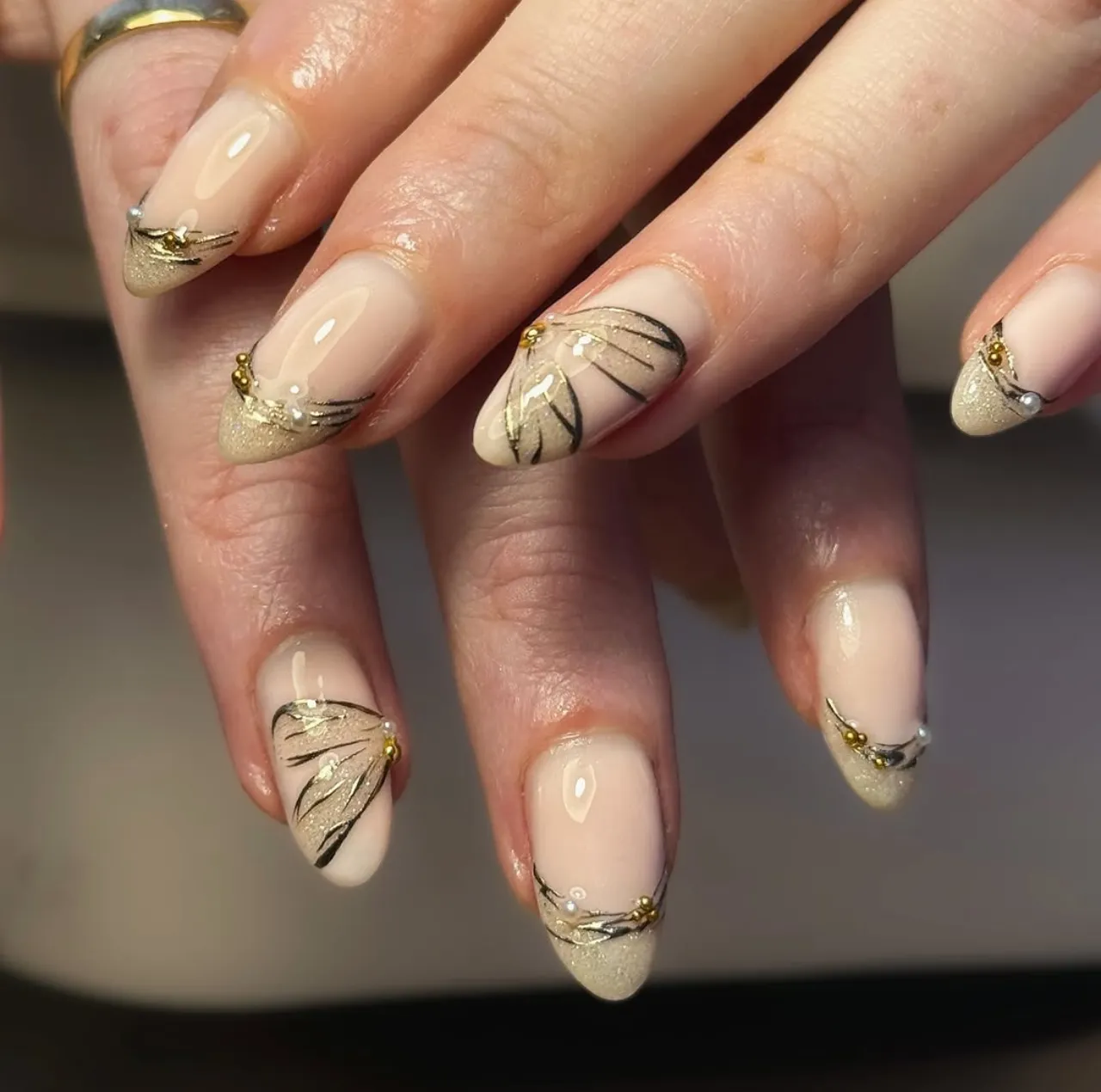 Diseños de uñas acrílicas con detalles de mariposa dorada y decoración brillante.