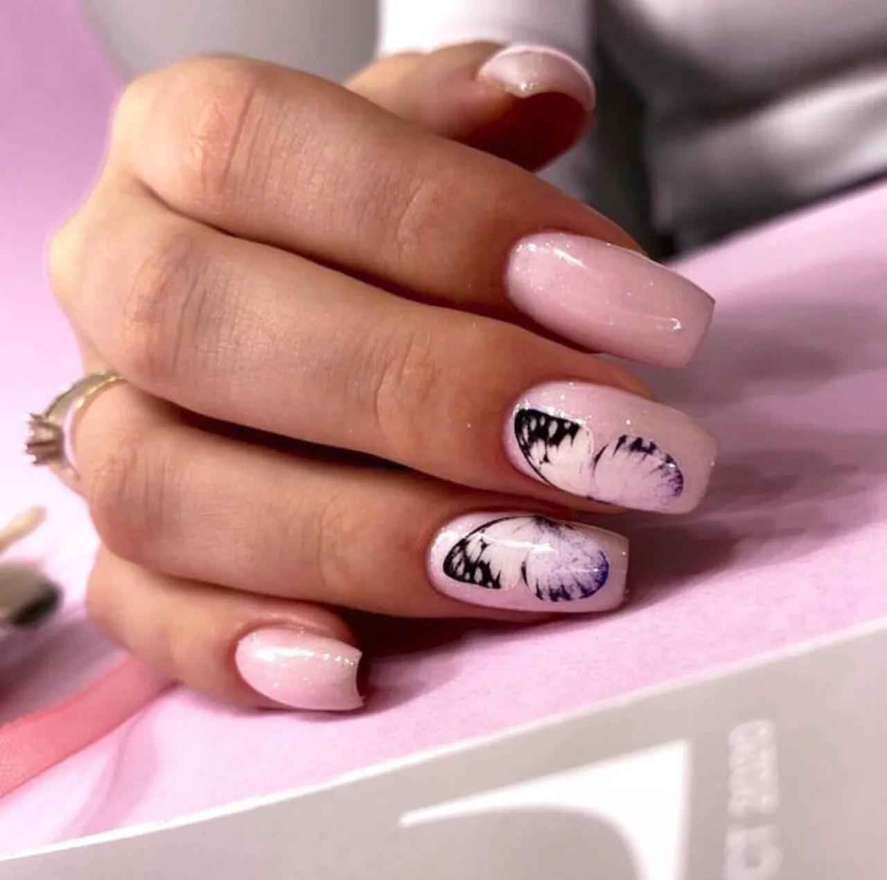 Diseños de uñas acrílicas rosadas con mariposa decorativa en estilo delicado y femenino.