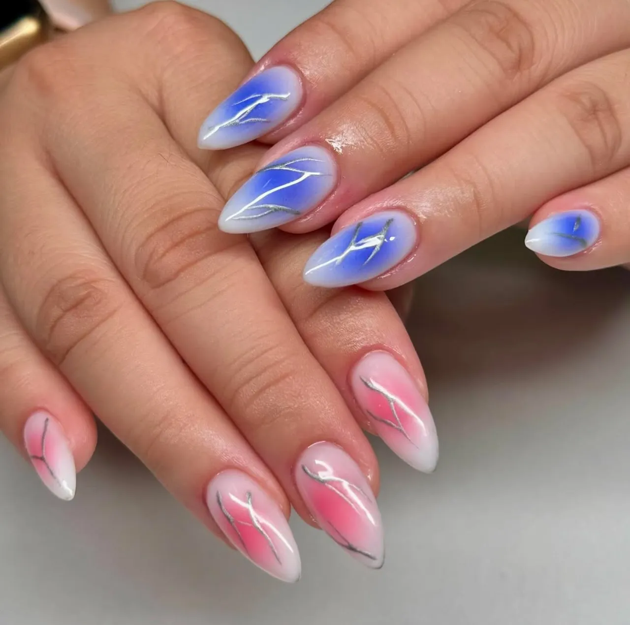 Efecto aura en uñas con degradado azul y rojo decorado con líneas metálicas.