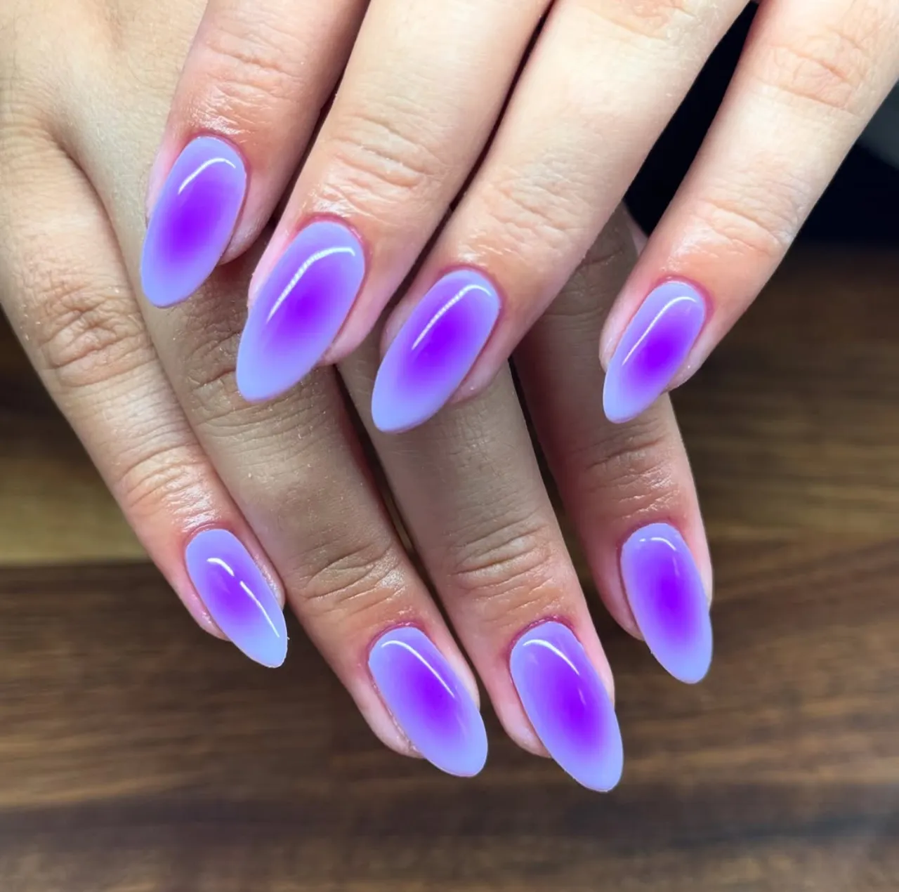 Efecto aura en uñas con tonos morados sobre base lavanda y acabado brillante.