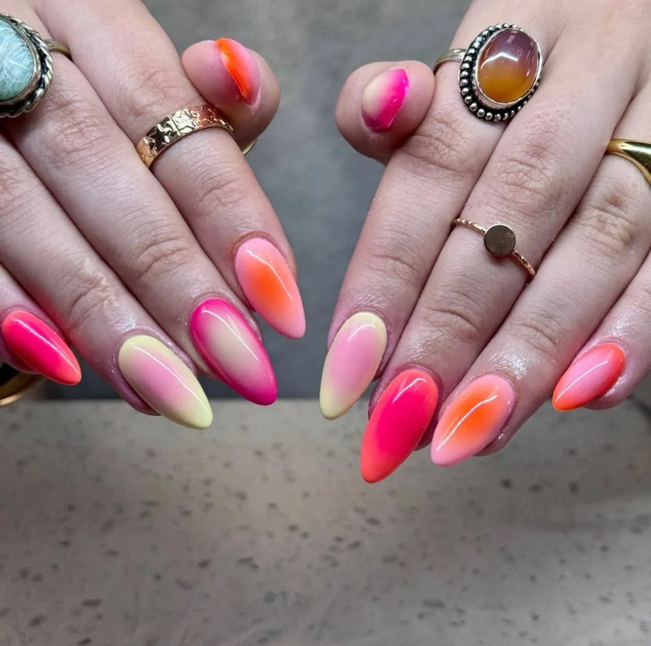 Diseño de uñas estilo efecto aura neón con tonos vibrantes rosa, naranja y amarillo.