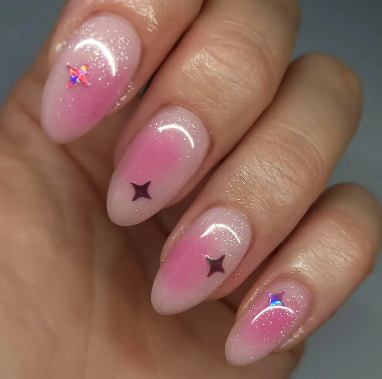Efecto aura en uñas con glitter rosado y decoraciones de estrellas holográficas.