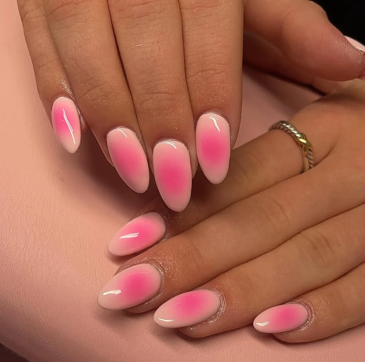 Efecto aura en uñas con degradado rosado sobre base clara y acabado brillante.