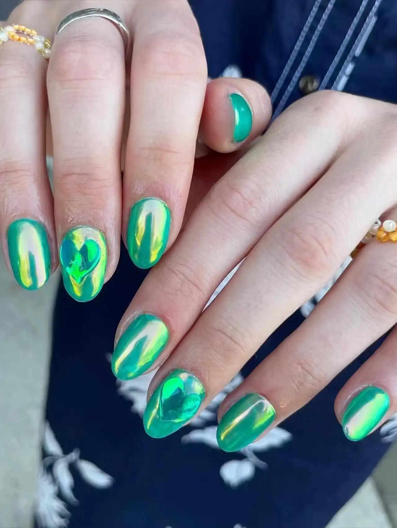 Green reflective chrome nails with heart accents showcasing aurora nail design ideas
