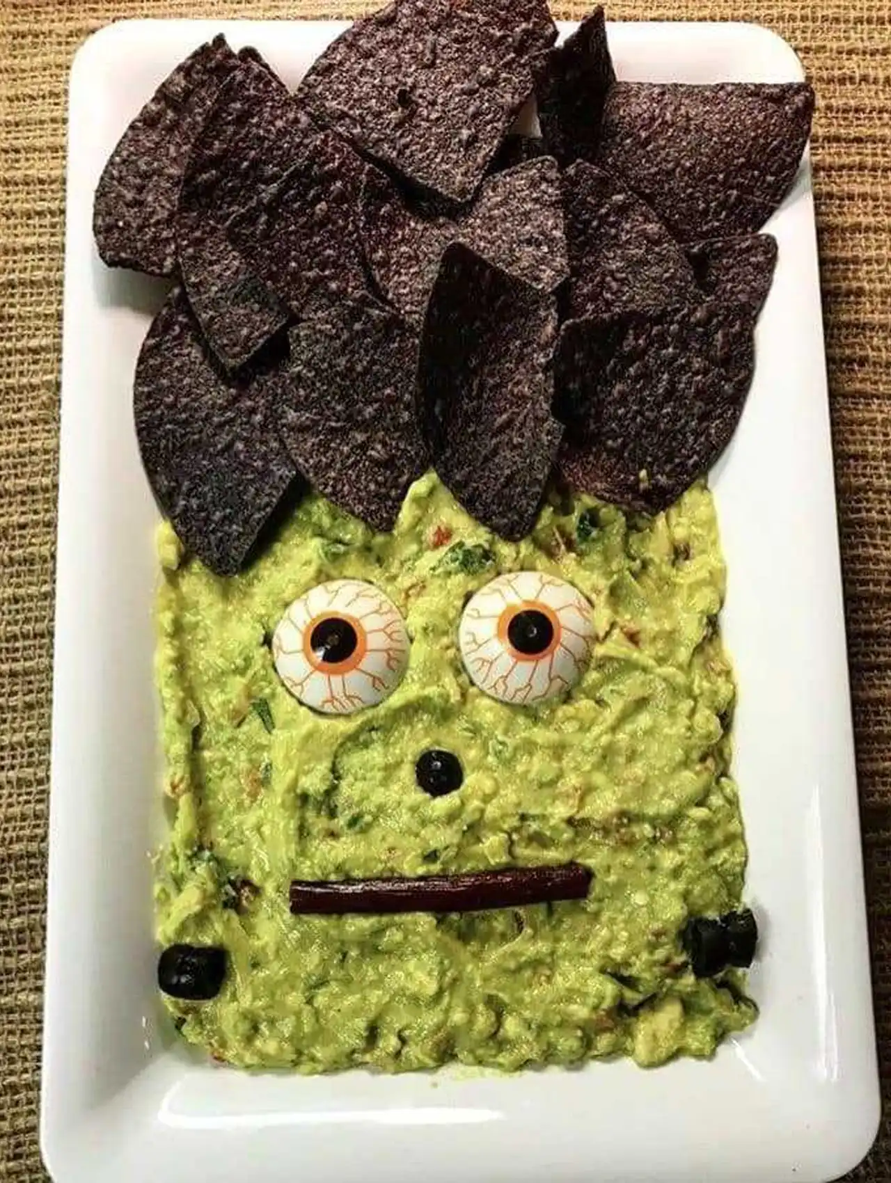 Frankenstein guacamole halloween charcuterie board with blue corn chips for hair.