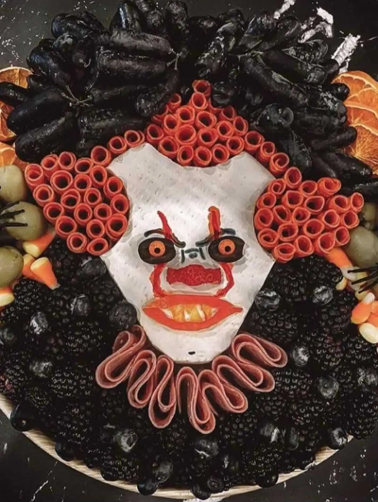 Pennywise IT clown halloween charcuterie board with meats, fruits, and cheese face.